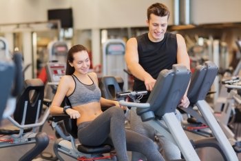 sport, fitness, lifestyle, technology and people concept - happy woman with trainer working out on exercise bike in gym