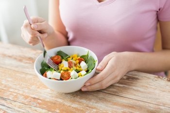 healthy eating, dieting and people concept - close up of young woman eating vegetable salad at home