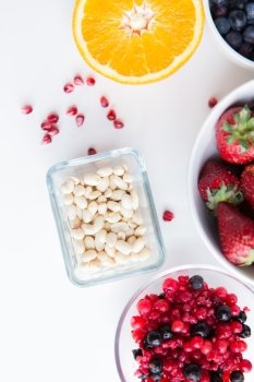 healthy eating, dieting, vegetarian food and people concept - close up of fruits, peanuts and berries in bowls on table
