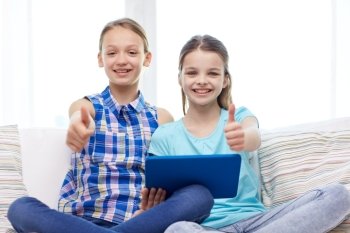 people, children, gesture, friends and friendship concept - happy little girls with tablet pc computer sitting on sofa and showing thumbs up at home