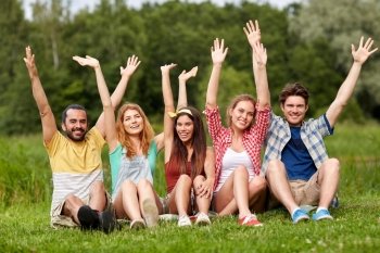 friendship, leisure, summer and people concept - group of smiling friends sitting on grass and waving hands outdoors
