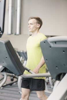 sport, fitness, lifestyle, technology and people concept - man with earphones exercising on treadmill in gym