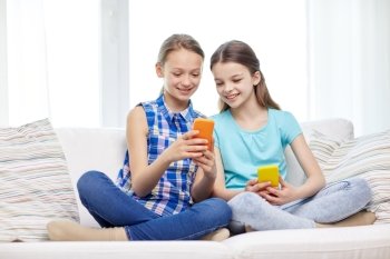 people, children, technology, friends and friendship concept - happy little girls with smartphones sitting on sofa at home