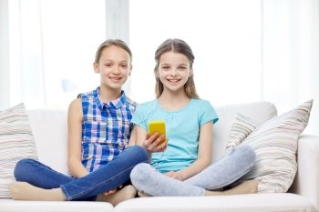 people, children, technology, friends and friendship concept - happy little girls with smartphone sitting on sofa at home