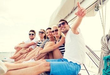 vacation, travel, sea, friendship and people concept - smiling friends sitting on yacht deck and pointing finger
