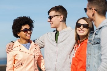 friendship, tourism, travel and people concept - group of happy teenage friends in sunglasses hugging and talking on city street