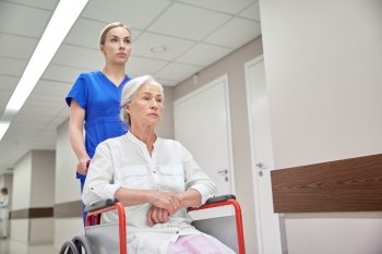 medicine, age, support, health care and people concept - nurse taking senior woman patient in wheelchair at hospital corridor