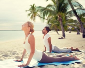 fitness, sport, yoga, people and lifestyle concept - happy couple making yoga exercises on tropical beach