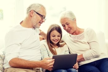 family, generation, technology and people concept - smiling grandfather, granddaughter and grandmother with tablet pc computer sitting on couch at home