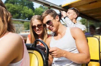 friendship, travel, vacation, summer and people concept - smiling couple in sunglasses with guidebook traveling by tour bus