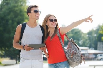 travel, tourism, summer vacation, technology and friendship concept - smiling couple with tablet pc and backpack pointing finger in city