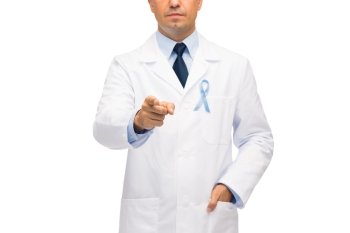 healthcare, profession, people and medicine concept - close up of male doctor in white coat with sky blue prostate cancer awareness ribbon pointing finger to you