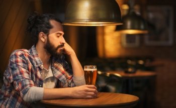 people, loneliness, alcohol and lifestyle concept - unhappy single man with beard drinking beer at bar or pub