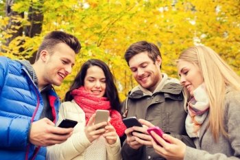 season, people, technology and friendship concept - group of smiling friends with smartphones in autumn park