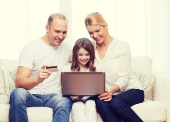 family, child, technology, money and home concept - smiling parents and little girl with laptop and credit card at home