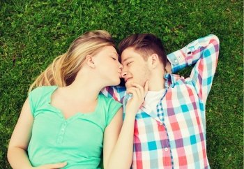 holidays, vacation, love and friendship concept - smiling couple lying on on grass and kissing in park