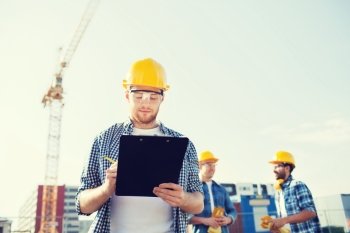 business, building, teamwork and people concept - group of builders in hardhats with clipboard outdoors