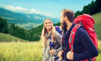 adventure, travel, tourism, hike and people concept - smiling couple walking with backpacks over alpine hills background