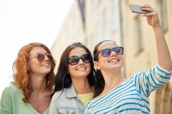 lifestyle, leisure, technology and people concept - smiling young women or teenage friends in sunglasses taking selfie with smartphone outdoors