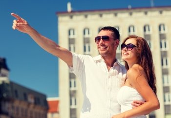 love, travel, tourism, people and friendship concept - smiling couple wearing sunglasses hugging and pointing finger in city
