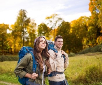adventure, travel, tourism, hike and people concept - smiling couple walking with backpacks over natural background