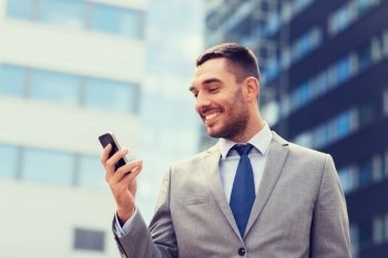 business, technology and people concept - smiling businessman with smartphone over office building