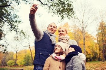 family, childhood, season, technology and people concept - happy family taking selfie with camera in autumn park