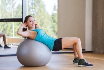 fitness, sport, training and people concept - smiling woman flexing abdominal muscles with exercise ball in gym