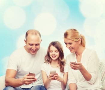 family, holidays, technology and people - smiling mother, father and little girl with smartphones over blue lights background