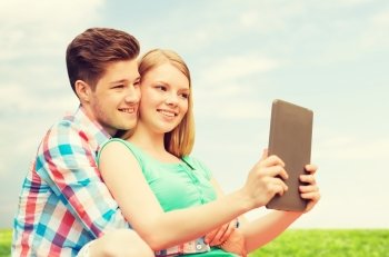 vacation, holidays, technology and love concept - smiling couple with tablet pc computer taking selfie over grass and blue sky background