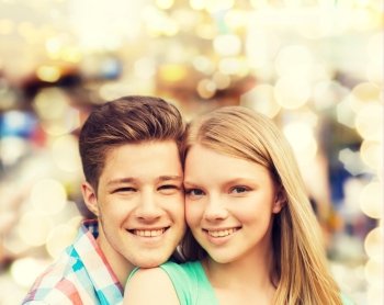 holidays, vacation, love and people concept - smiling teenage couple hugging over holiday lights background