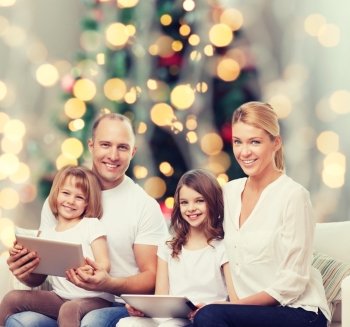 family, holidays, technology and people - smiling mother, father and little girls with tablet pc computers over christmas tree lights background