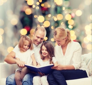 family, childhood, holidays and people - smiling mother, father and little girls reading book over living room and christmas tree lights background