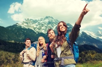 adventure, travel, tourism, hike and people concept - group of smiling friends with backpacks pointing finger over alpine mountains background