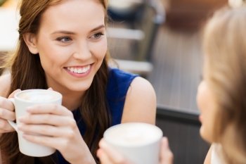 communication and friendship concept - smiling young women with coffee cups at cafe. smiling young women with coffee cups at cafe