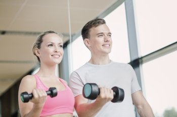 fitness, sport, exercising and diet concept - smiling young woman and personal trainer with dumbbells in gym