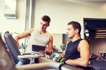 sport, fitness, equipment, technology and people concept - men with tablet pc computer exercising on gym machine
