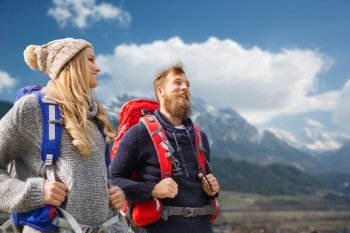 adventure, travel, tourism, hike and people concept - smiling couple walking with backpacks over mountains background
