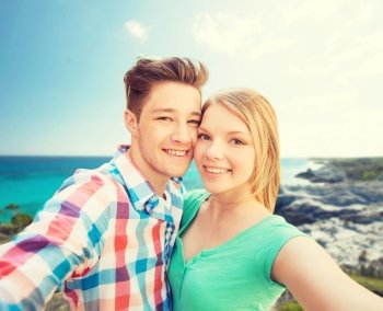 people, love, vacation, technology and summer concept - happy couple taking selfie with smartphone or camera over sea shore background