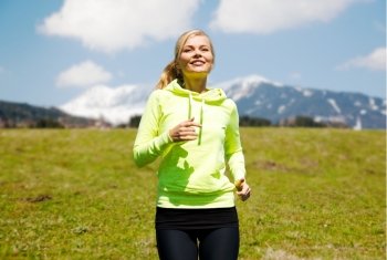 fitness, sport, people and healthy lifestyle concept - happy young smiling woman jogging or running  over mountains, green field and blue sky background