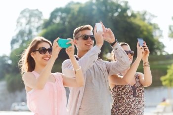 friendship, leisure, summer, technology and people concept - group of smiling friends with smartphone taking picture outdoors