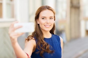 technology and people concept - happy young woman with smartphone taking selfie on city street. happy woman taking selfie with smartphone in city