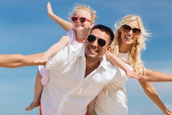 family, summer vacation, adoption and people concept - happy man, woman and little girl in sunglasses having fun over blue sky background