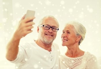 family, technology, age and people concept - happy senior couple with smartphone taking selfie at home