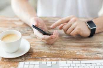 business, technology and people concept - close up of male hand holding smart phone and wearing watch with coffee and keyboard at wooden table