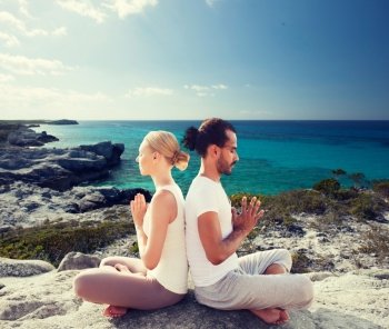 fitness, sport, yoga, people and lifestyle concept - happy couple sitting in lotus pose on beach