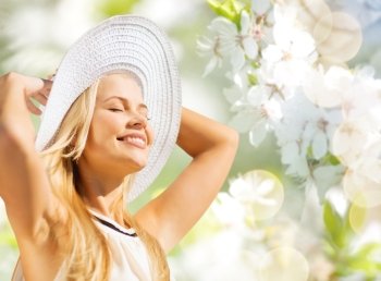 fashion, people and summer holidays concept - beautiful woman in hat and dress sunbathing over green blooming garden background