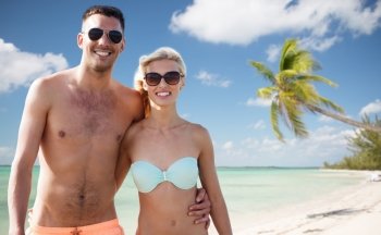 love, travel, tourism, summer and people concept - smiling couple on vacation in swimwear and sunglasses hugging over tropical beach background
