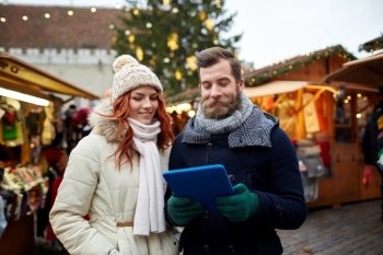 holidays, winter, christmas, technology and people concept - happy couple of tourists in warm clothes with tablet pc computer walking in old town