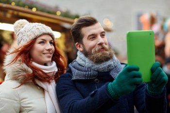 holidays, winter, christmas, technology and people concept - happy couple of tourists in warm clothes taking selfie with tablet pc computer walking in old town